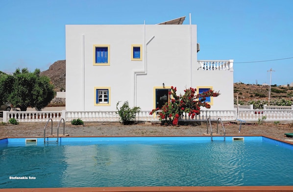 A white building with blue trim and a swimming pool in front.
