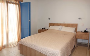 A hotel room with a bed, bedside tables, a nightstand, a blue door, and a curtain.