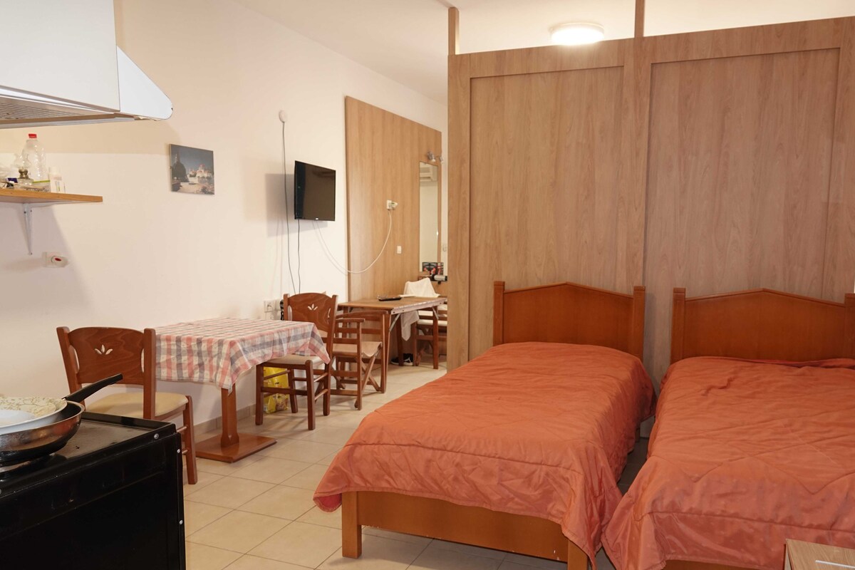 A bedroom with two beds, a desk, a chair, a TV, and a microwave.
