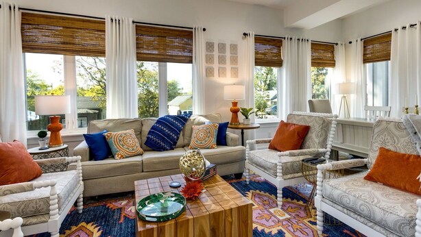 A well-lit living room with a beige sofa, two armchairs, a coffee table, and a patterned rug. Large windows with white curtains and wooden blinds provide natural light. - Luxury@Dwell /Rooftop With Views/ Mins to Downtown (Nashville)