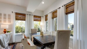 A dining area with a wooden table and chairs, white curtains, and a view of trees and buildings outside. - Luxury@Dwell /Rooftop With Views/ Mins to Downtown (Nashville)