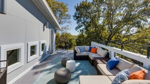 A modern outdoor living area with a sofa set, round ottomans, and a view of trees. - Luxury@Dwell /Rooftop With Views/ Mins to Downtown (Nashville)