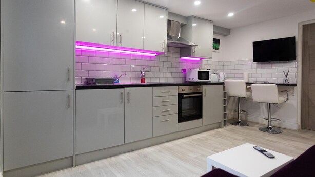 A modern kitchen with grey cabinets, a microwave, and a TV mounted on the wall. - Westwood Apartment (Leeds)