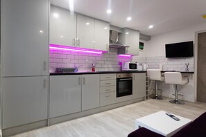 Une cuisine moderne avec des meubles gris, un four à micro-ondes et un téléviseur fixé au mur.