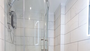 A modern bathroom with a glass-enclosed shower, a white sink, and marble tiles. - Westwood Apartment (Leeds)