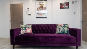 A purple velvet sofa with floral cushions, a framed movie poster, and a telephone on the wall. - Westwood Apartment (Leeds)