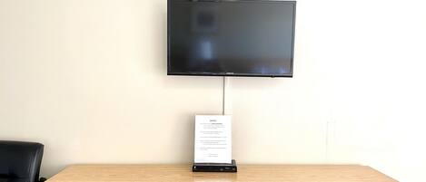 A flat-screen TV mounted on a wall above a wooden desk with drawers.
