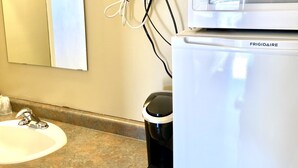 Un baño con lavamanos, espejo y un refrigerador blanco con la etiqueta "FRIGIDAIRE".