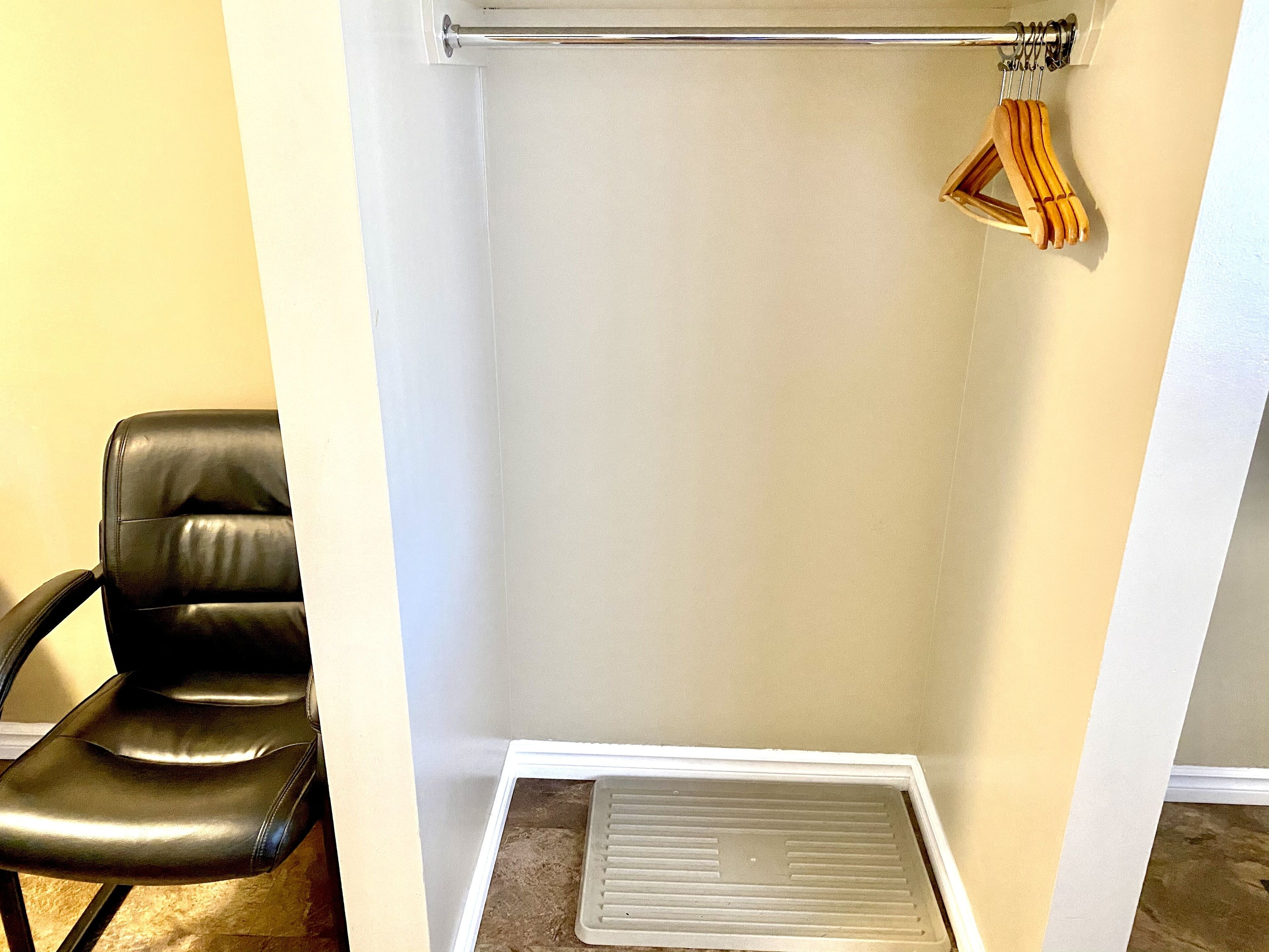 A corner of a room with a black leather chair, a white baseboard, and a metal vent.