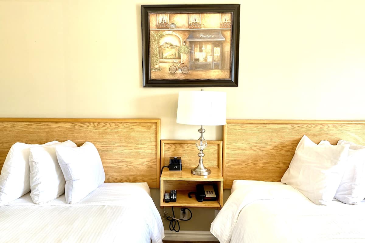 Ein Hotelzimmer mit zwei Betten, einem Nachttisch mit Lampe, einem Telefon und einem gerahmten Bild an der Wand.