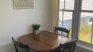 Un coin repas avec une table en bois et quatre chaises, une plante en pot et une fenêtre avec des rideaux.