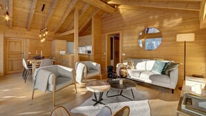 A cozy wooden cabin interior with a dining area, a living room with a sofa and chairs, and a kitchen area. - Dorealp - superb apartment for 6 in peaceful setting - OVO Network (La Clusaz)