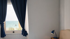 Habitación de hotel con cama, mesita de noche, lámpara, ventana con cortinas y aire acondicionado.