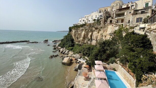 Un hotel frente al mar con piscina, edificios de piedra y costa rocosa.