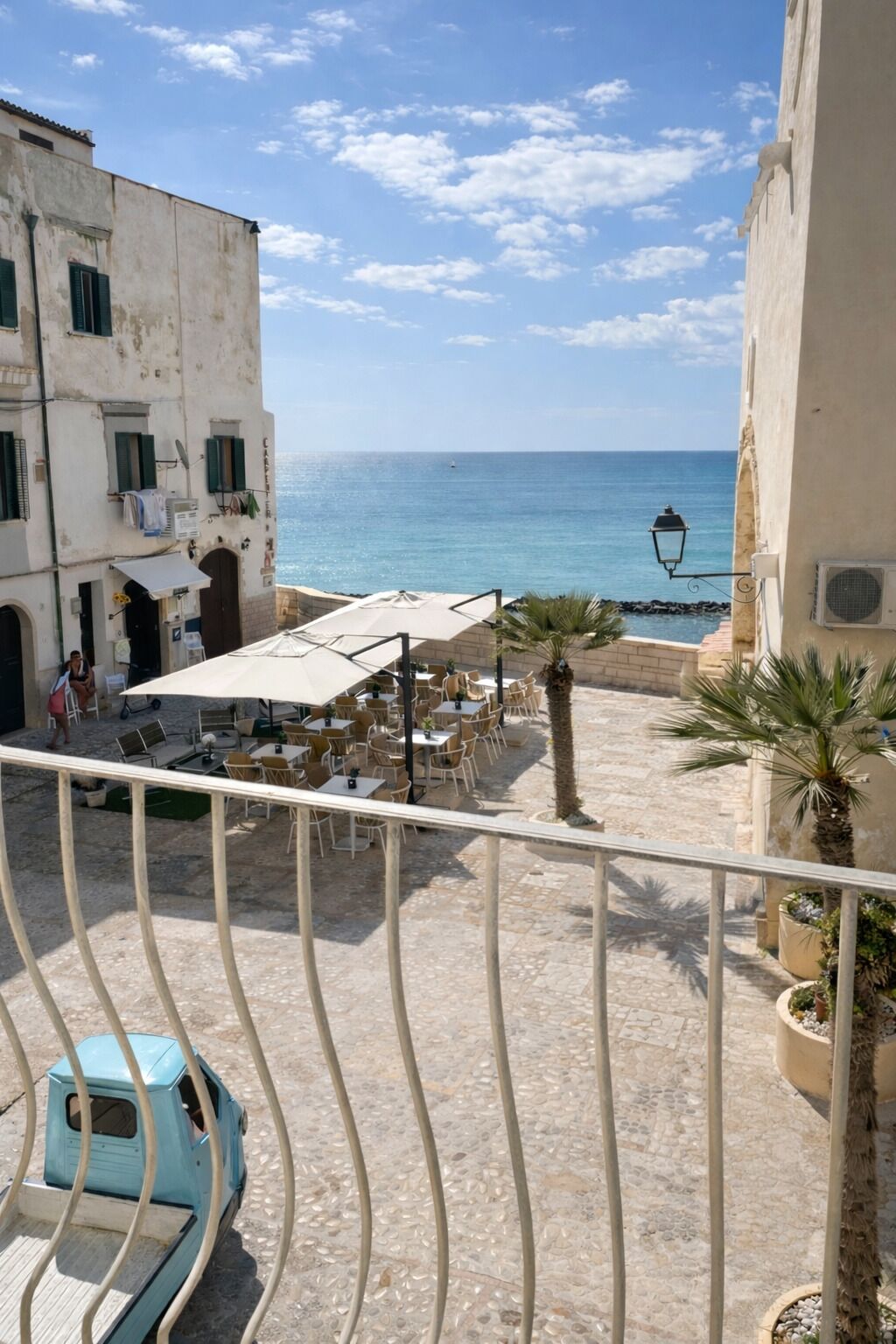 Una terraza con mesas al aire libre, vista al mar y un edificio con balcón.