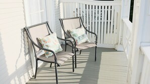 Dos sillones de mimbre con cojines estampados en una terraza de madera con barandillas blancas.