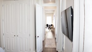 Un pasillo con puertas blancas, un televisor de pantalla plana montado en la pared y un comedor al fondo.