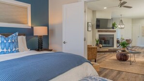 Un dormitorio con cama, mesita de noche, lámpara y vista al área de estar.