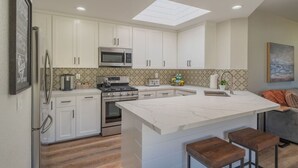 Una cocina moderna con armarios blancos, una isla grande, un microondas, una estufa y un tragaluz.
