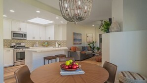 Una cocina moderna con armarios blancos, una isla central y una zona de comedor con una mesa redonda y sillas.
