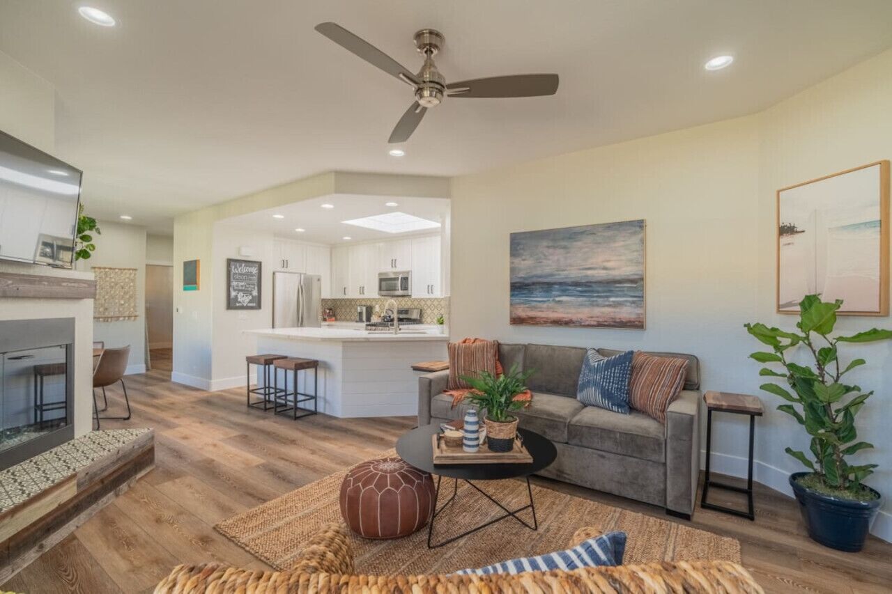 A modern living room with a fireplace, a sofa, a coffee table, and a dining area with a kitchen in the background.