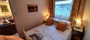 Una cama bien hecha con almohadas, una lámpara de noche y una ventana con cortinas.