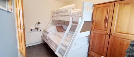 A bunk bed room with a wooden wardrobe and a desk with a lamp.