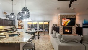 Et moderne køkken med hængende lamper, et spiseområde med udsigt, en pejs og en stue med en sofa.