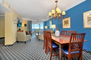 A dining area with a wooden table and chairs, a chandelier, and a view of the ocean through a large window. - 2BR/2BA Unobstructed ocean view in Dunes Village (Myrtle Beach)