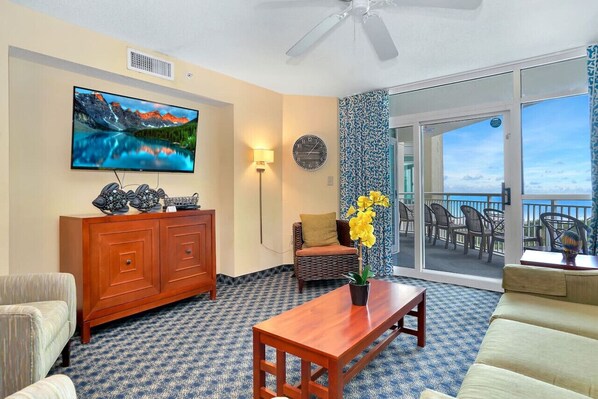A living room with a television, a wooden cabinet, a sofa, a coffee table, and a balcony with outdoor furniture. - 2BR/2BA Unobstructed ocean view in Dunes Village (Myrtle Beach)