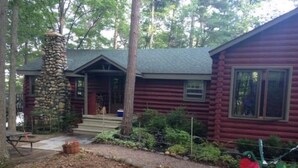 A log cabin with a stone chimney, a porch, and a small garden area with potted plants. - Traverse City @ Rennie Lake  .. Idyllic Lakefront Retreat ..  CC49 ... Perfect! (traverse city)