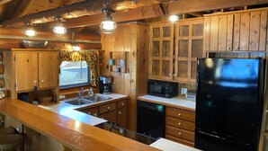 A wooden cabin-style kitchen with a large island, built-in appliances, and a window with a curtain. - Traverse City @ Rennie Lake  .. Idyllic Lakefront Retreat ..  CC49 ... Perfect! (traverse city)