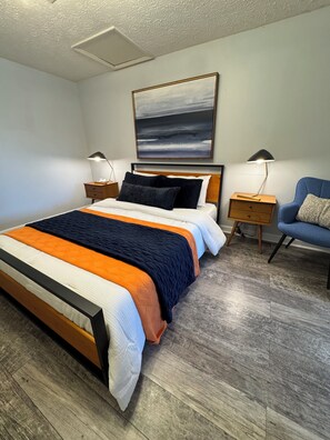 A neatly arranged bedroom with a bed, bedside tables, a chair, and a painting on the wall.