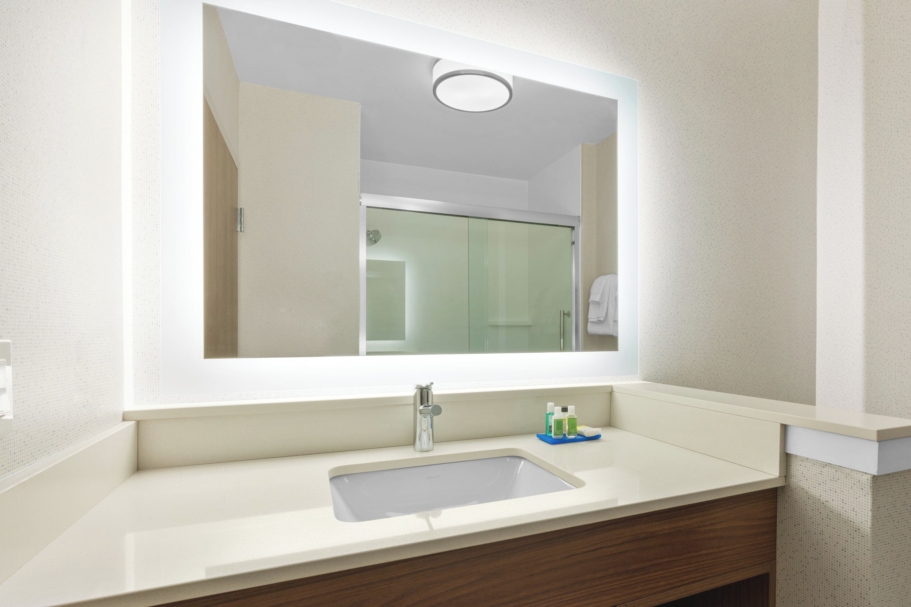 A bathroom with a large mirror, a sink, and a shower visible in the reflection.