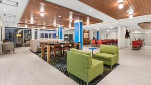 A spacious lobby with a wooden ceiling, a seating area with green and red chairs, and a large window overlooking the street. - Holiday Inn Express & Suites Suisun City by IHG (Suisun City)