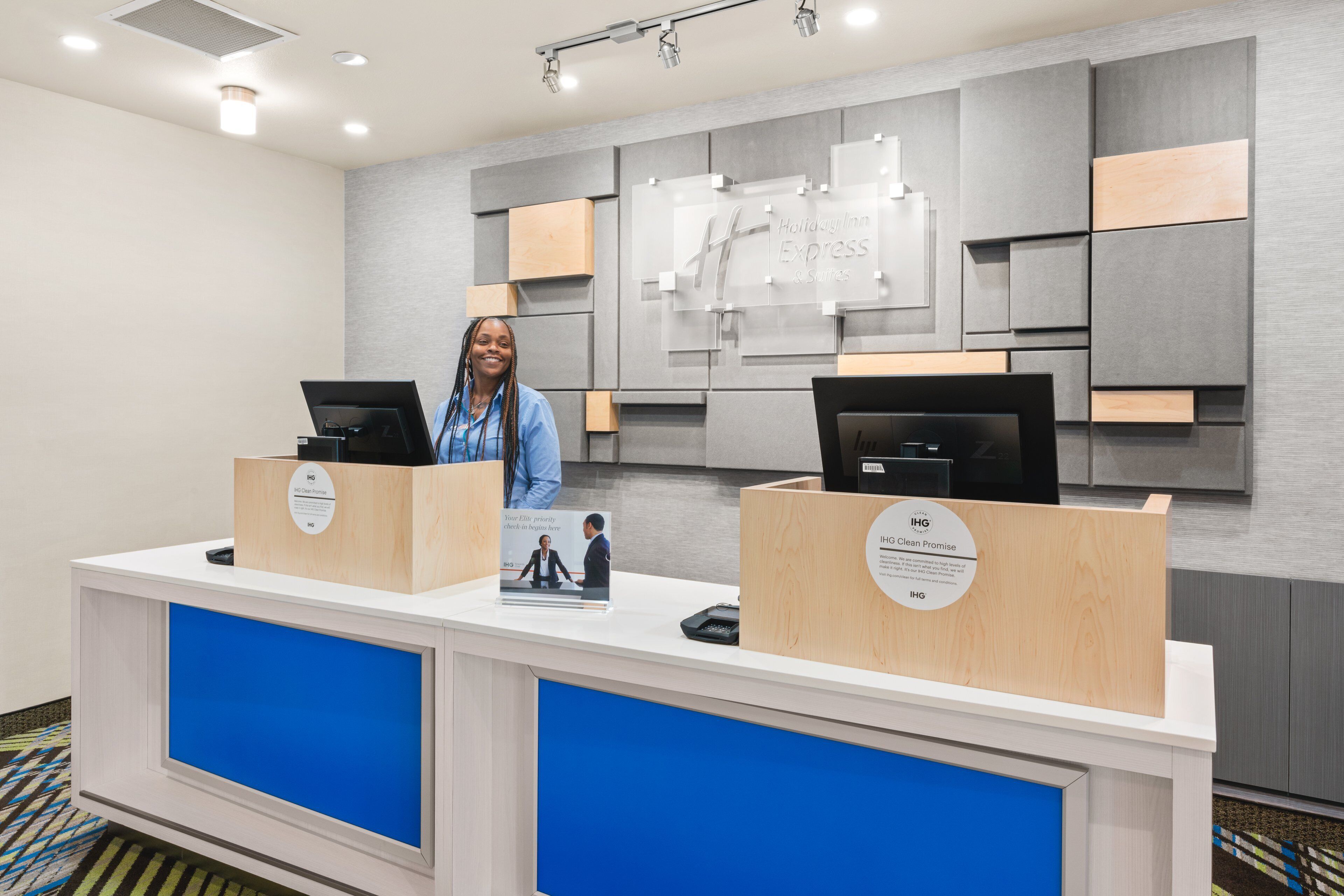 En receptionsdisk med två datorarbetsplatser, en blå accentvägg och en stor skylt med hotellets namn.