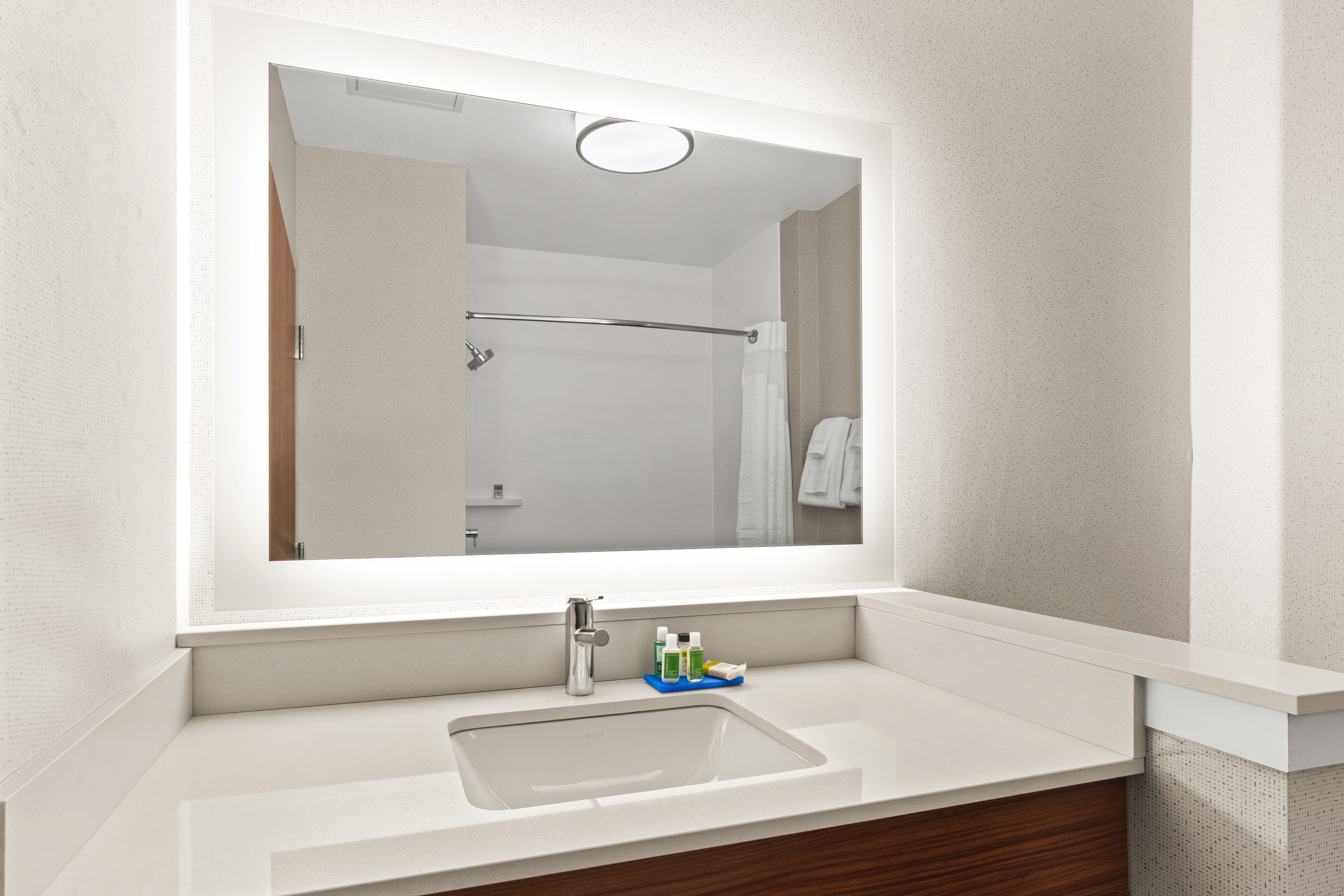 A modern bathroom with a large mirror, a white sink, and a wooden vanity.
