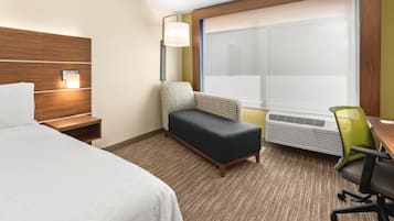 Habitación de hotel con cama, escritorio, silla, banco, lámpara de pared y ventana con persianas.