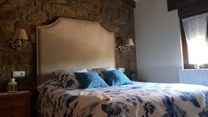 A bedroom with a stone wall, a wooden headboard, a floral bedspread, and two blue pillows. - Place of peace. (Arroyo de Valdearroyo)