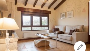 A cozy living room with a sofa, a coffee table, and a lamp. There is a window with a view of trees and a radiator under the window. - Place of peace. (Arroyo de Valdearroyo)