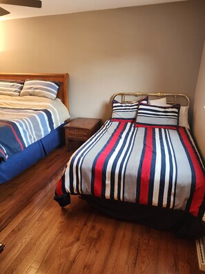 Un dormitorio con dos camas, suelo de madera y una mesita de noche.