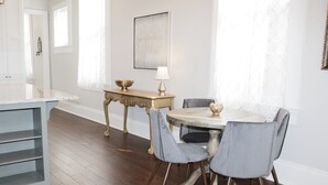 A dining area with a round table, four chairs, a small side table with a lamp, and a decorative bowl. - Elegant Historic 1906 2BR • Balcony • Lower Garden District (New Orleans)