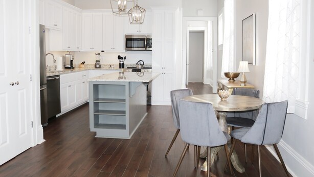 A modern kitchen with white cabinetry, a central island, and a dining area with grey chairs. - Elegant Historic 1906 2BR • Balcony • Lower Garden District (New Orleans)