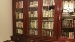 A room with a large wooden bookcase filled with books, a wooden chair with a floral cushion, and a wooden bench. - Villa Camilla Guest House - Appartamento 1 (Reggio Calabria)