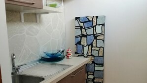 A compact kitchen with a sink, a stove, and a small countertop. There is a decorative wall piece and a lamp on the wall. - Villa Camilla Guest House - Appartamento 1 (Reggio Calabria)