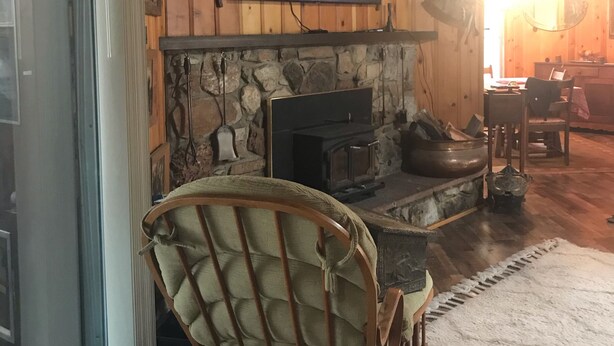 Un salon chaleureux avec une cheminée en pierre, un téléviseur fixé au mur et un fauteuil en bois.