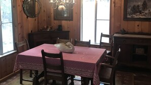 Un coin repas avec une table dressée pour quatre personnes, entourée de chaises en bois. Un lustre est suspendu au plafond et un grand miroir est fixé au mur.