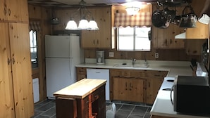 Une cuisine dotée de meubles en bois, d’un îlot central, d’un réfrigérateur, d’un four à micro-ondes et d’un évier.