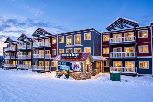 Ein mehrstöckiges Hotel mit Balkonen, einer Steinfassade und einem Schild für 'Mountain Lodge' und 'Ice Rink'.