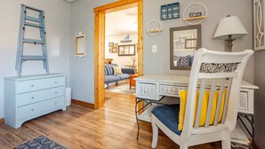 A room with a wooden ladder, a white dresser, a desk, a white chair with yellow cushions, and a lamp.